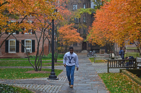 Student in Yale sweatshirt walking on old campus, fall
